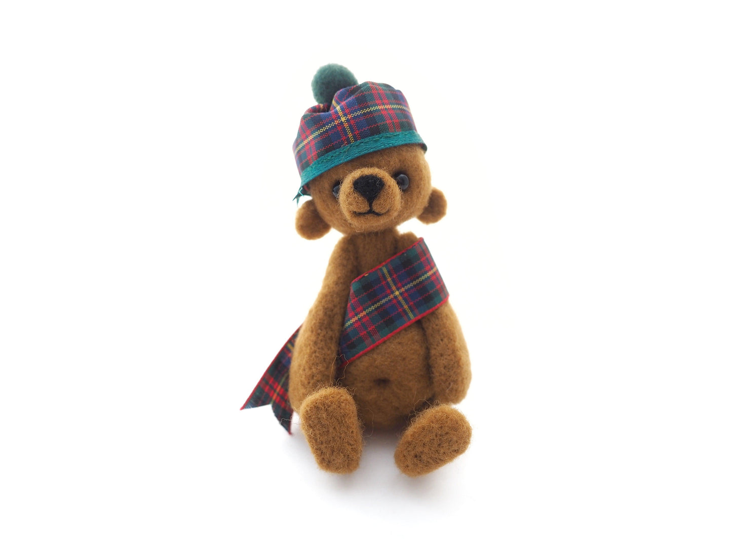 A small needle felted bear with a tartan hat and sash