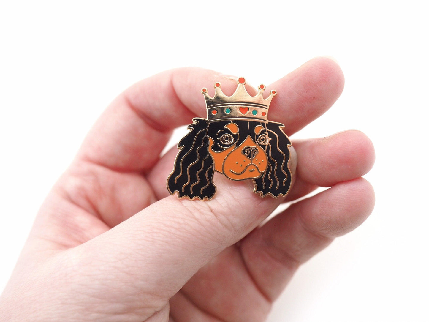 A photo of a hand holding a Black and Tan Cavaloer King Charles enamel pin