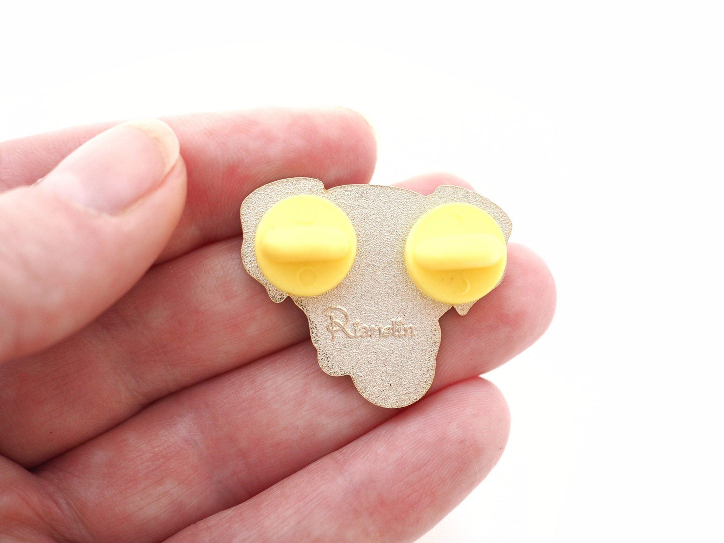 A photo of the back of a Boxer dog enamel pin, with 2 yellow rubber clutch fastenings